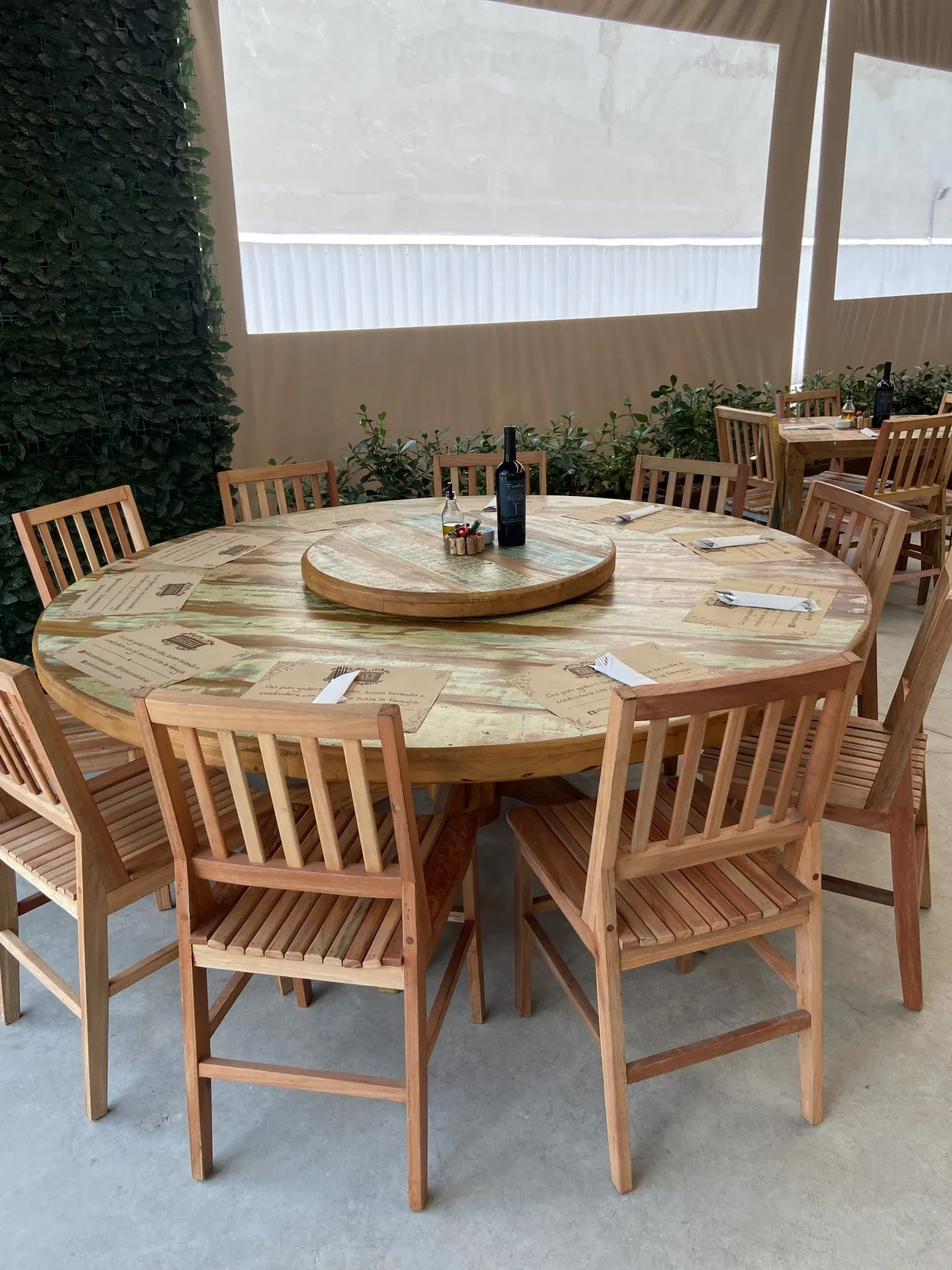 Quintal Gastronômico Piazzale com mesa redonda de madeira de demolição, prato giratório e cadeiras rústicas