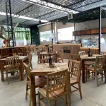 Visão ampla do ambiente com mesas e cadeiras em madeira de demolição no Quintal Gastronômico Piazzale