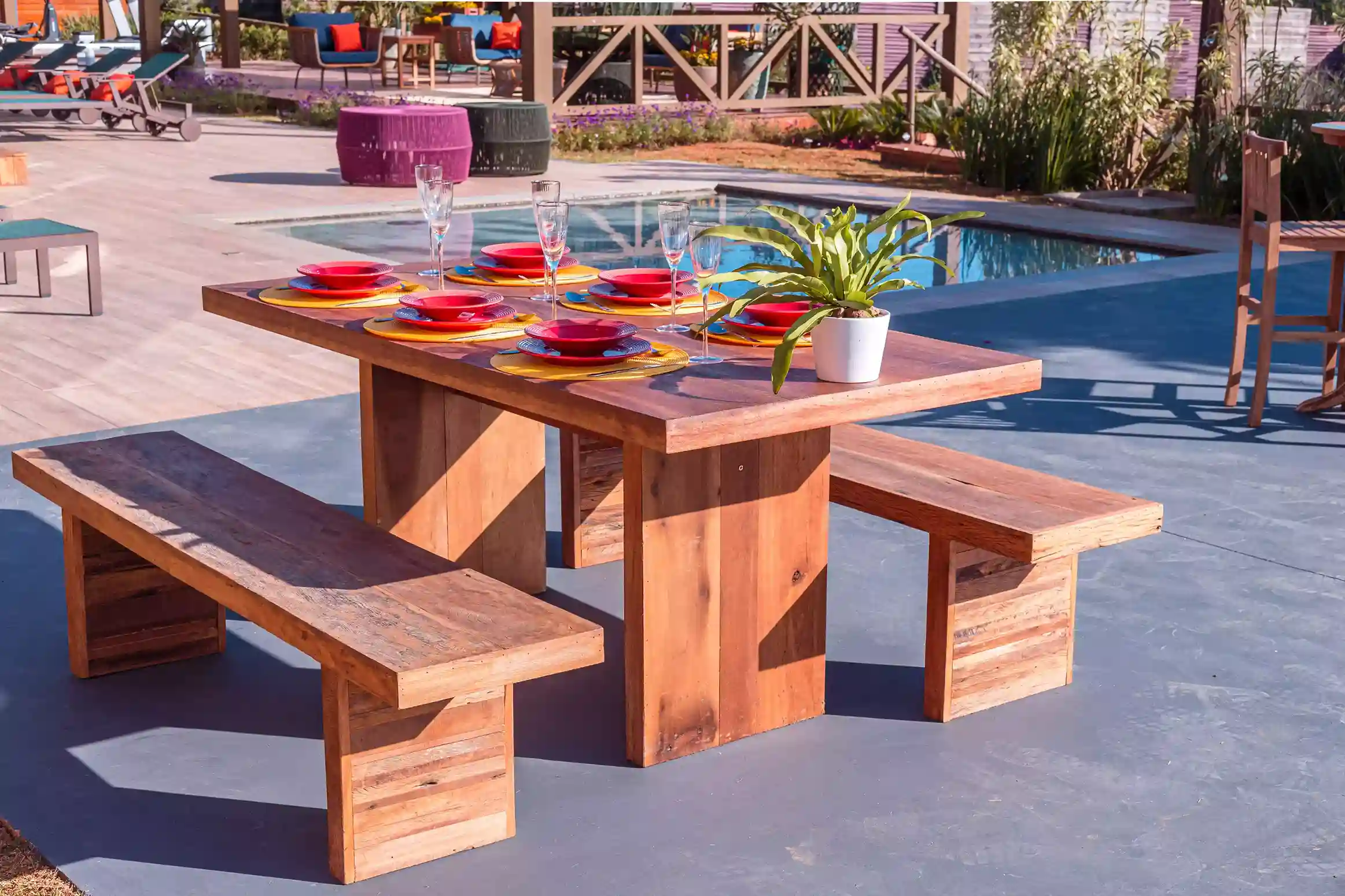 Mesa de madeira Canela com pés em estilo painel, acompanhada de bancos no mesmo modelo, como vista no programa Power Couple da TV Record