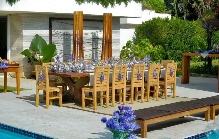 Cadeiras de madeira de demolição em mesa posta ao lado da piscina, em ambiente externo