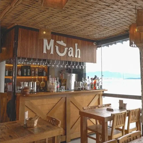 Mesas e cadeiras rústicas no Muah Bar – móveis da madeira de demolição com aplicação real em ambiente comercial Ambiente do Muah Bar com mesas e cadeiras em madeira de demolição, decoração rústica real de bar com a logo